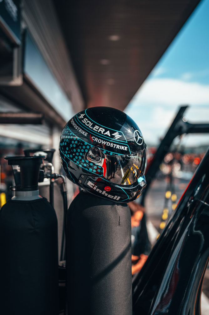 Un casco del equipo Mercedes-AMG PETRONAS Formula One Team, con los logotipos de los patrocinadores claramente visibles —entre ellos Einhell, CrowdStrike y Solera—, está colocado sobre un balón de gas en la calle de boxes. El reflejo en la visera muestra el entorno del garaje.