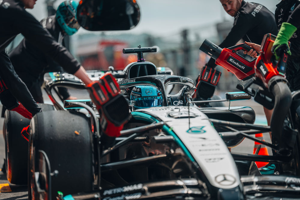 Un auto del equipo Mercedes-AMG PETRONAS Formula One durante una parada en boxes. Los miembros del equipo utilizan sopladoras inalámbricas Einhell para enfriar los componentes del vehículo. El equipo está concentrado y trabaja con precisión.