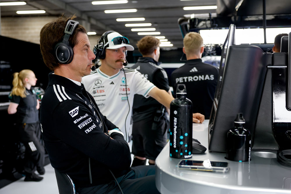 Toto Wolff y Valtteri Bottas, del equipo Mercedes-AMG PETRONAS Formula One Team, están en la estación de trabajo del equipo dentro del garaje. Se enfocan en la estrategia de carrera, observan los monitores y se comunican mediante audífonos.