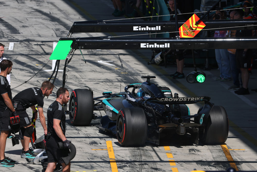 Un auto del equipo Mercedes-AMG PETRONAS Formula One está en la calle de boxes durante una parada. Varios miembros del equipo rodean el auto. El logo de Einhell es visible sobre el área de boxes.